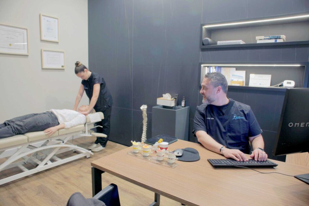 ajuste-quiropractico-en-consulta-almeria Quiropráctica realizando un ajuste a una cliente mientras otro profesional supervisa la consulta en Almería Quiropráctica