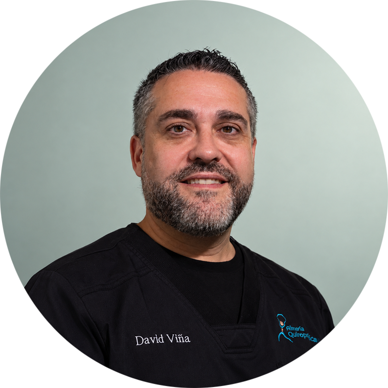 David Viña, profesional de Almería Quiropráctica, sonriente y con uniforme negro, sobre un fondo verde claro